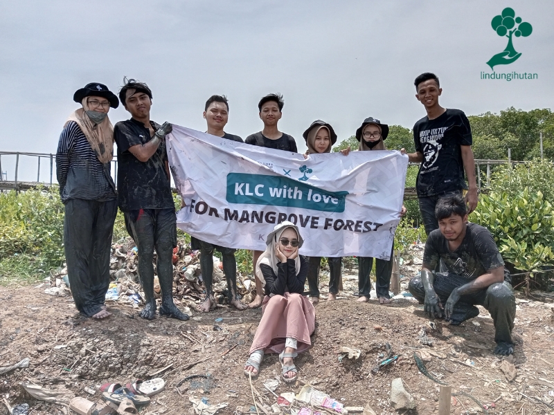 Foto bersama dengan banner kegiatan Klamby di lokasi penanaman mangrove.